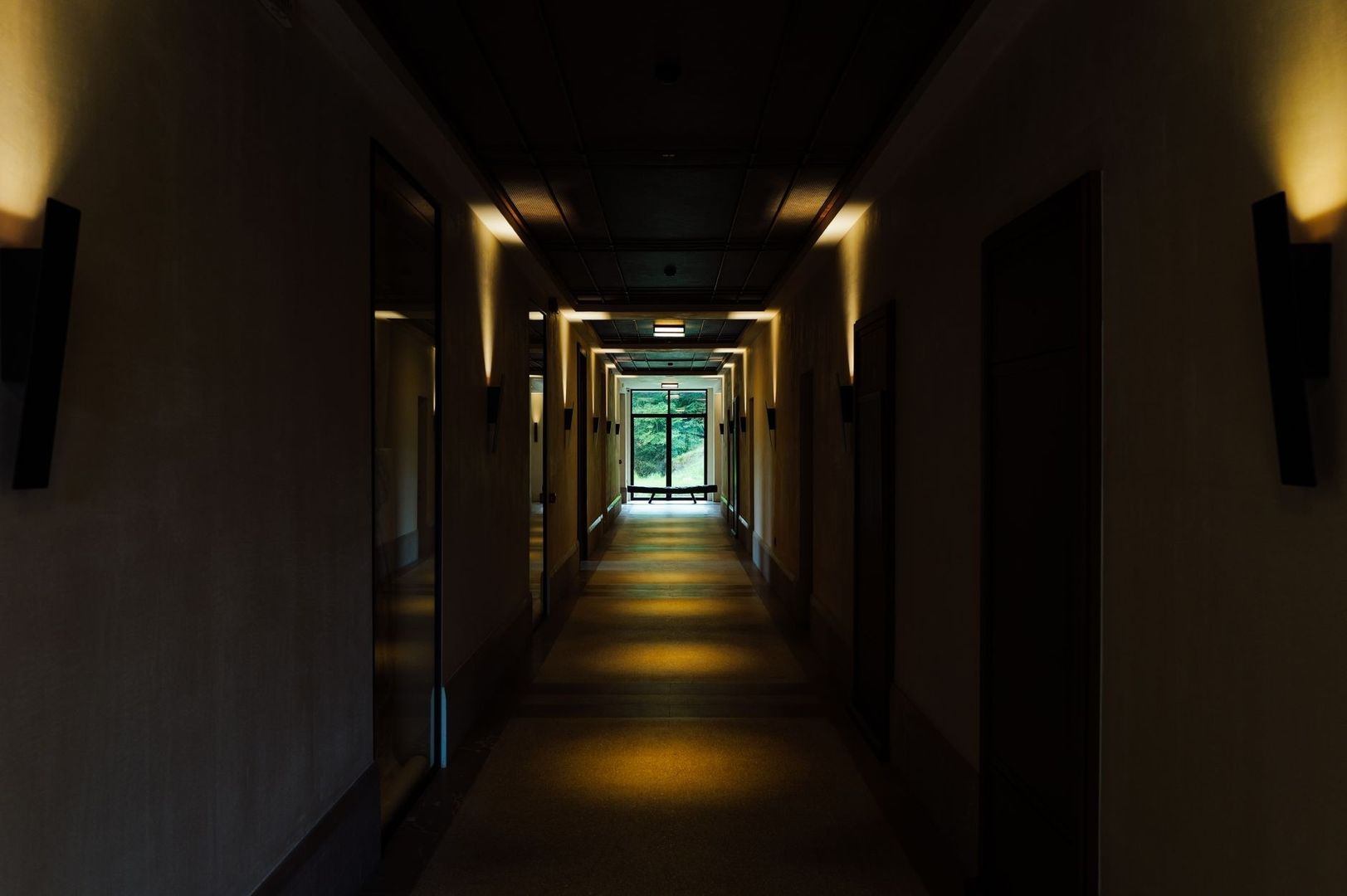Dunkler, langer Hotelkorridor mit warmem Licht und Fenster am Ende