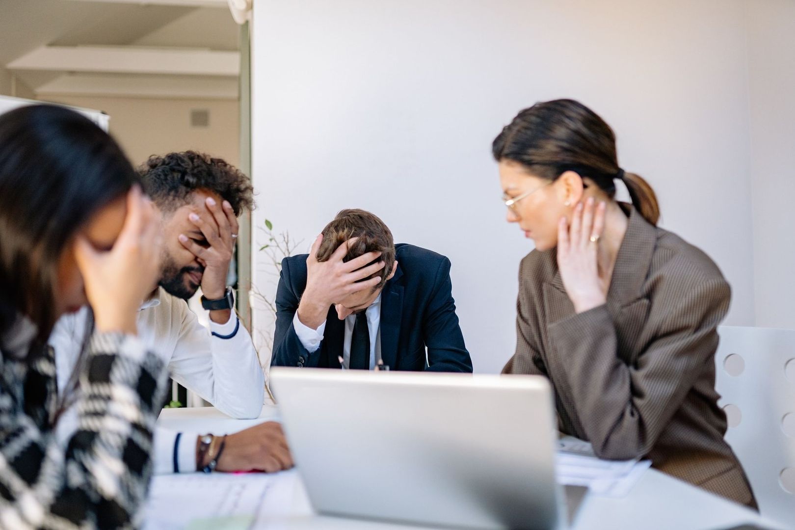 Vier Geschäftsleute sitzen angespannt an einem Tisch mit Laptop