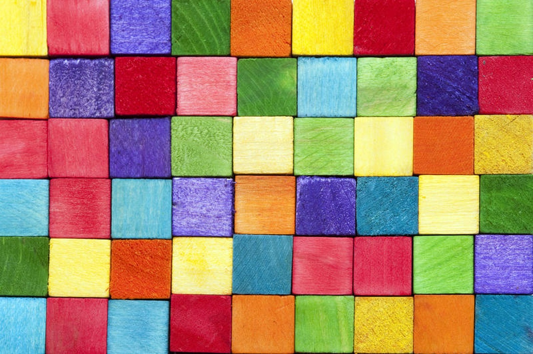 Ein farbenfrohes Gitter aus bemalten Holzklötzen in Rot, Blau, Gelb und anderen leuchtenden Farben.